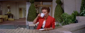 Movie still from “Daddy Long Legs” (1955), directed by Jean Negulesco – A woman in a red jacket drinking from a cup; Medium shot, High angle