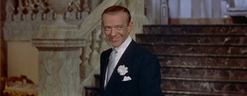 A man wearing a suit and tie standing in front of a staircase