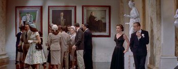 Movie still from “Daddy Long Legs” (1955), directed by Jean Negulesco – A group of people standing in front of paintings; Wide shot, Over the shoulder angle