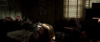 Movie still from “The Hills Have Eyes” (2006), directed by Alexandre Aja – A cat laying on top of a bed in a dark room; Wide shot, High angle