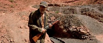 Movie still from “The Hills Have Eyes” (2006), directed by Alexandre Aja – An older man holding a rifle on a rocky hillside; Medium shot, High angle