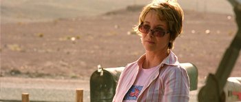 Movie still from “The Hills Have Eyes” (2006), directed by Alexandre Aja – A woman wearing sunglasses and a pink shirt is standing near a mailbox; Close Up shot, Over the shoulder angle