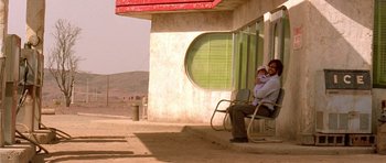 Movie still from “The Hills Have Eyes” (2006), directed by Alexandre Aja – A man and a baby sitting on a bench outside; Wide shot, Low angle