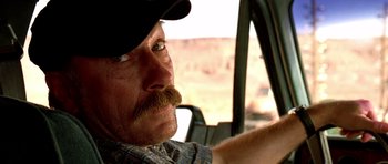 Movie still from “The Hills Have Eyes” (2006), directed by Alexandre Aja – A person driving a car wearing a hat; Close Up shot, Over the shoulder angle