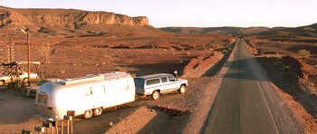 Movie still from “The Hills Have Eyes” (2006), directed by Alexandre Aja – An suv towing a trailer on a dirt road in the middle of the desert; Extreme Wide shot, Low angle