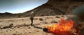 Movie still from “The Hills Have Eyes” (2006), directed by Alexandre Aja – A woman is standing in the desert next to a burning tire; Wide shot, Low angle