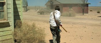 Movie still from “The Hills Have Eyes” (2006), directed by Alexandre Aja – A man holding a baseball bat walking across a dirt field; Wide shot, Over the shoulder angle