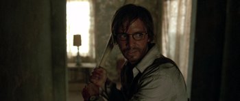 Movie still from “The Hills Have Eyes” (2006), directed by Alexandre Aja – A man holding a sword while wearing glasses and a tie; Close Up shot, Over the shoulder angle