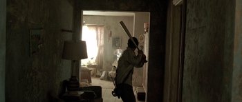 Movie still from “The Hills Have Eyes” (2006), directed by Alexandre Aja – A person holding a baseball bat in a room; Wide shot, Low angle