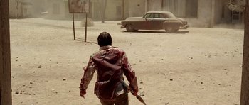 Movie still from “The Hills Have Eyes” (2006), directed by Alexandre Aja – A person walking in the dirt holding a knife; Wide shot, Over the shoulder angle