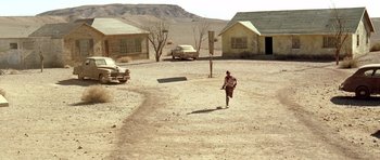 Movie still from “The Hills Have Eyes” (2006), directed by Alexandre Aja – A man running across a dirt field near some houses; Extreme Wide shot, High angle