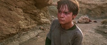 Movie still from “The Hills Have Eyes” (2006), directed by Alexandre Aja – A young man is standing in the dirt near rocks; Close Up shot, High angle