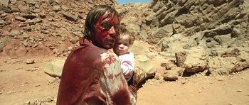 Movie still from “The Hills Have Eyes” (2006), directed by Alexandre Aja – A man holding a baby in his arms and covered in blood; Medium shot, High angle
