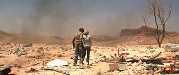 Movie still from “The Hills Have Eyes” (2006), directed by Alexandre Aja – A couple of people standing on top of a dirt field; Wide shot, Over the shoulder angle