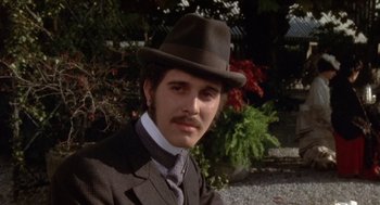Movie still from “Daisy Miller” (1974), directed by Peter Bogdanovich – A man wearing a suit and a hat in front of some bushes; Close Up shot, Low angle