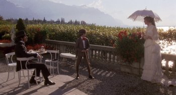 Movie still from “Daisy Miller” (1974), directed by Peter Bogdanovich – A man in a suit and tie standing in front of a table; Wide shot, Over the shoulder angle