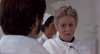 Movie still from “Daisy Miller” (1974), directed by Peter Bogdanovich – A group of people standing next to each other in a room; Close Up shot, Over the shoulder angle