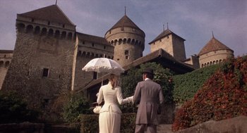 Movie still from “Daisy Miller” (1974), directed by Peter Bogdanovich – A man and a woman holding hands while standing in front of a castle; Wide shot, Low angle