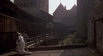 Movie still from “Daisy Miller” (1974), directed by Peter Bogdanovich – A man walking down a street near a bridge; Wide shot, High angle