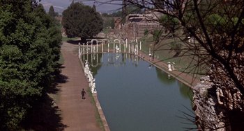 Movie still from “Daisy Miller” (1974), directed by Peter Bogdanovich – A man walking down a path next to a body of water; Extreme Wide shot, High angle