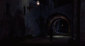 Movie still from “Daisy Miller” (1974), directed by Peter Bogdanovich – A person standing in the dark under a street light; Wide shot, High angle