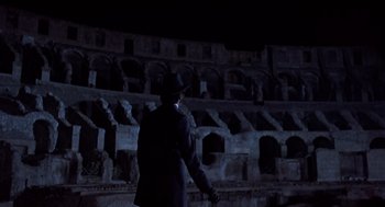 Movie still from “Daisy Miller” (1974), directed by Peter Bogdanovich – A man in a suit and a hat standing in front of an arena; Wide shot, Low angle