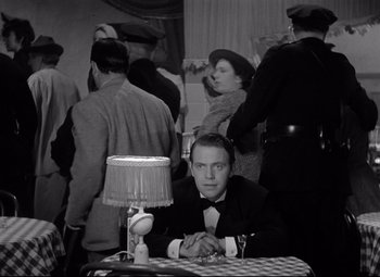 Movie still from “Dance, Girl, Dance” (1940), directed by Roy Del Ruth – A black and white photo of a man sitting at a table; Medium shot, High angle