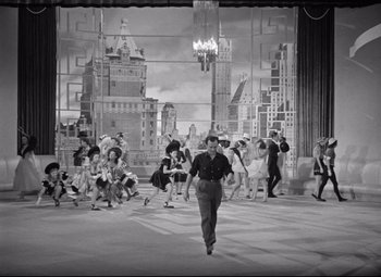 Movie still from “Dance, Girl, Dance” (1940), directed by Roy Del Ruth – A black and white photo of a man walking in front of a group of people; Extreme Wide shot, High angle