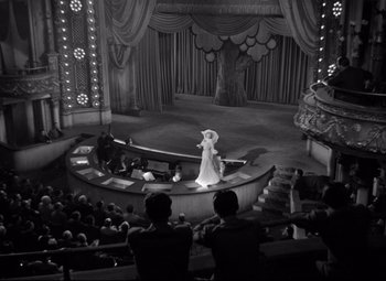 Movie still from “Dance, Girl, Dance” (1940), directed by Roy Del Ruth – A woman in a white dress is on a stage; Extreme Wide shot, High angle