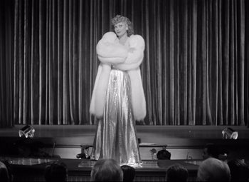 Movie still from “Dance, Girl, Dance” (1940), directed by Roy Del Ruth – An old photo of a woman in a silver dress and a fur coat; Wide shot, Low angle