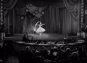 Movie still from “Dance, Girl, Dance” (1940), directed by Roy Del Ruth – A woman in a white dress is performing a dance on a stage; Extreme Wide shot, High angle