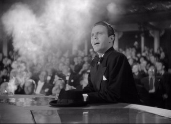 Movie still from “Dance, Girl, Dance” (1940), directed by Roy Del Ruth – A man in a suit and hat sitting in front of an audience; Medium shot, Low angle