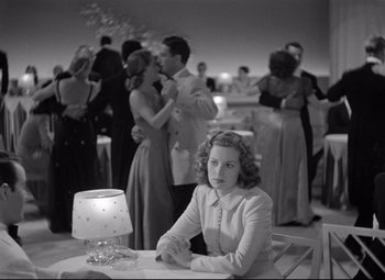 Movie still from “Dance, Girl, Dance” (1940), directed by Roy Del Ruth – A black and white photo of a woman sitting at a table in front of other people; Wide shot, Over the shoulder angle