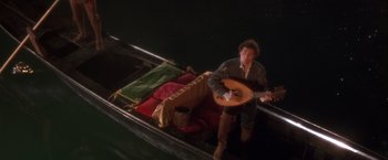 Movie still from “Dangerous Beauty” (1998), directed by Marshall Herskovitz – A man sitting in a boat holding a guitar; Wide shot, High angle