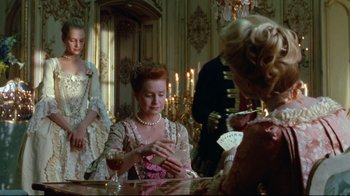 Movie still from “Dangerous Liaisons” (1988), directed by Stephen Frears – A woman in a pink dress playing cards in a room; Medium shot, Over the shoulder angle