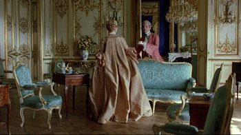 Movie still from “Dangerous Liaisons” (1988), directed by Stephen Frears – A woman in an old - fashioned dress stands in front of a mirror in an ornate room; Wide shot, Over the shoulder angle