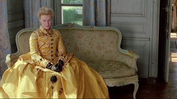 Movie still from “Dangerous Liaisons” (1988), directed by Stephen Frears – A woman in a yellow dress sitting on a couch; Medium shot, Low angle