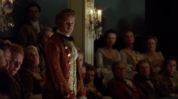 Movie still from “Dangerous Liaisons” (1988), directed by Stephen Frears – A man standing in front of a group of people in a room; Medium shot, Over the shoulder angle