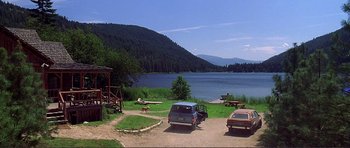 Movie still from “Dante's Peak” (1997), directed by Roger Donaldson – A group of cars parked on a dirt road near a body of water; Extreme Wide shot, High angle