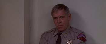 Movie still from “Dante's Peak” (1997), directed by Roger Donaldson – A man in a sheriff's uniform stares into the camera; Close Up shot, Low angle