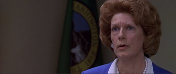 Movie still from “Dante's Peak” (1997), directed by Roger Donaldson – An older woman in front of the washington state seal; Close Up shot, Low angle