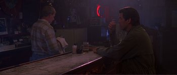 Movie still from “Dante's Peak” (1997), directed by Roger Donaldson – A man sitting at a bar with a drink in his hand; Medium shot, Over the shoulder angle
