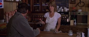 Movie still from “Dante's Peak” (1997), directed by Roger Donaldson – A woman in a white apron is holding a glass of red wine; Medium shot, Over the shoulder angle
