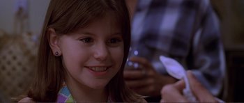 Movie still from “Dante's Peak” (1997), directed by Roger Donaldson – A little girl smiling for the camera while holding a cell phone; Close Up shot, Over the shoulder angle