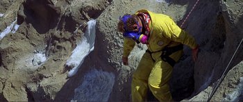 Movie still from “Dante's Peak” (1997), directed by Roger Donaldson – A man in a yellow suit is climbing a mountain; Wide shot, High angle