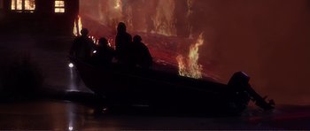 Movie still from “Dante's Peak” (1997), directed by Roger Donaldson – A group of people sitting in a boat in front of a fire; Extreme Wide shot, High angle