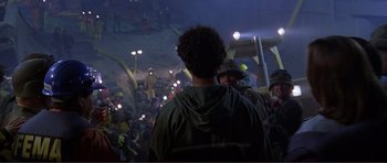 Movie still from “Dante's Peak” (1997), directed by Roger Donaldson – A crowd of people standing in a dark room at night; Medium shot, Over the shoulder angle