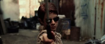 Movie still from “Daredevil” (2003), directed by Mark Steven Johnson – A young boy wearing sunglasses and holding a gun; Close Up shot, Low angle