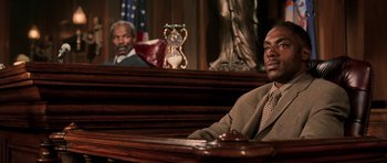 Movie still from “Daredevil” (2003), directed by Mark Steven Johnson – A man sitting in a courtroom with another man in the background; Medium shot, Low angle