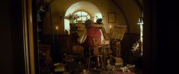 Movie still from “The Hobbit: An Unexpected Journey” (2012), directed by Peter Jackson – An old woman sitting in a chair in front of an open book case; Wide shot, High angle